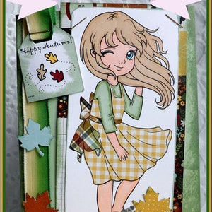 May include: A card with a cartoon girl with blonde hair and a yellow and white checkered dress. The card has a green ribbon with a tag that says "Happy Autumn!" and a green background with fall leaves. The card also has a small cartoon girl with brown hair and a floral design. The text "Designed by Deanne Saunders littlebitpaper.blogspot.com Lemon Shortbread" is at the bottom of the card.
