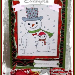 May include: A green card with a white border and a red and black patterned border. The card features a hand-drawn illustration of two snowmen. The larger snowman is wearing a gray top hat with red and green lights, a red bow tie, and a green scarf. The smaller snowman is wearing a red hat and a red and white striped scarf. The card has the text "Example" at the top and "warm winter wishes" at the bottom. The card also has the text "Designed by Deanne Saunders" and "littlepaper-blogspot.com Lemon Shortbread" at the bottom.