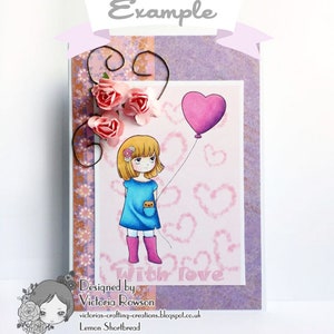 May include: A handmade card with a purple background and a pink heart balloon. A girl with blonde hair and a blue dress is holding the string of the balloon. The card has a pink and brown patterned border and the text "Designed by Victoria Rowson" and "With love" in pink letters.