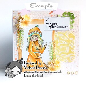 May include: A handmade greeting card with a girl wearing a yellow and orange outfit and a hat. The card has a white frame with the text "Enjoy your birthday" inside. The background is a light orange with white splatters.