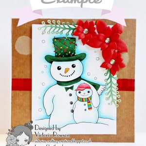 May include: A Christmas card featuring a snowman with a green hat and a smaller snowman with a red hat. The card is decorated with red flowers and green leaves. The text on the card reads "Designed by Victoria Rowson, victorias-crafting-creations.blogspot.co.uk, Lemon Shortbread".