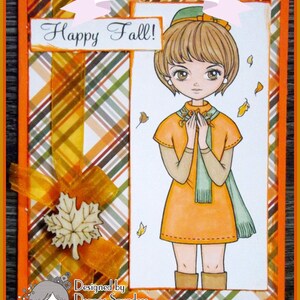 Peut inclure: Une carte sur le th&egrave;me de l'automne avec une fille en robe marron et &eacute;charpe verte, tenant un bouquet de fleurs. L'arri&egrave;re-plan est un motif &agrave; carreaux orange, marron et blanc. La carte dit "Happy Fall!" et "Designed by Deanne Saunders".
