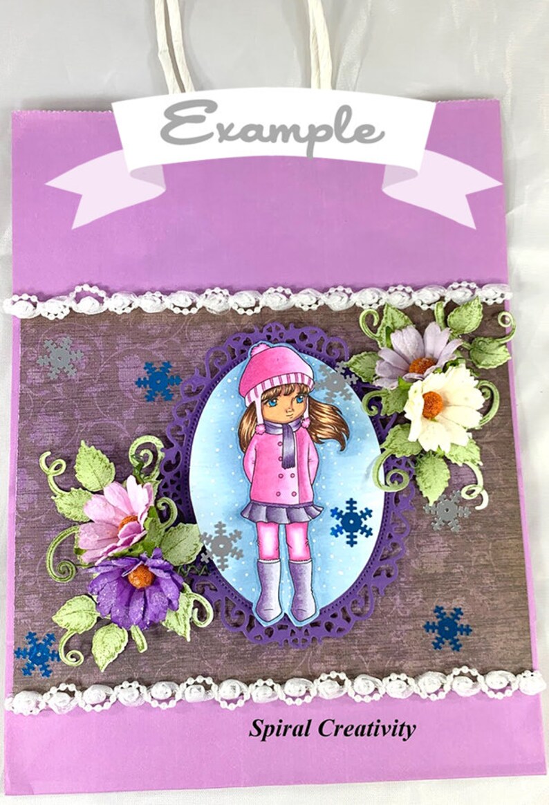May include: A purple gift bag with a white lace trim and a white ribbon with the word "Example" printed on it. The bag features a brown background with a girl wearing a pink coat and a white hat standing in a purple oval frame. The girl is surrounded by snowflakes and flowers. The bag also has the text "Spiral Creativity" printed on the bottom.
