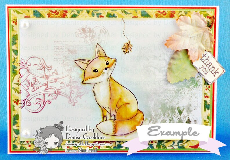 May include: A card with a watercolor illustration of a fox sitting on a white background. The fox is orange and white with a bushy tail. The card has a floral border and the text "Designed by Denise Goeldner" and "Example" on it.