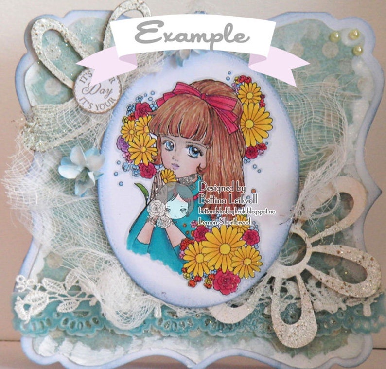 May include: A white card with a blue border and a white oval in the center. The oval contains a drawing of a girl with long brown hair wearing a blue dress and a red bow. She is holding a small doll with blonde hair. The oval is surrounded by flowers and the text "Designed by Bettina Leikvoll bettinahobbykrock.blogspot.ne Lemon Shortbread". The card also has a white ribbon with the text "Example" on it.