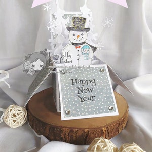 May include: A pop-up card with a snowman and a smaller snowman holding hands. The card is decorated with snowflakes and the words "Happy New Year" on the front.