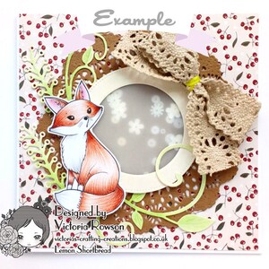 May include: A handmade card featuring a fox illustration with a brown, white, and orange color scheme. The fox is surrounded by a brown doily, green leaves, and a white circle with a lace bow. The card has a white background with a red berry pattern.