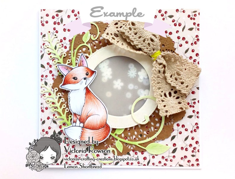 May include: A handmade card featuring a fox illustration with a brown, white, and orange color scheme. The fox is surrounded by a brown doily, green leaves, and a white circle with a lace bow. The card has a white background with a red berry pattern.