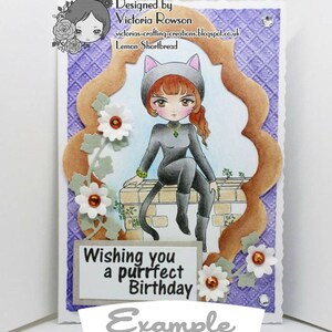 May include: A purple card with a white and orange flower design. The card features a cartoon cat wearing a black catsuit and a cat hat. The text on the card reads "Wishing you a purrfect Birthday".