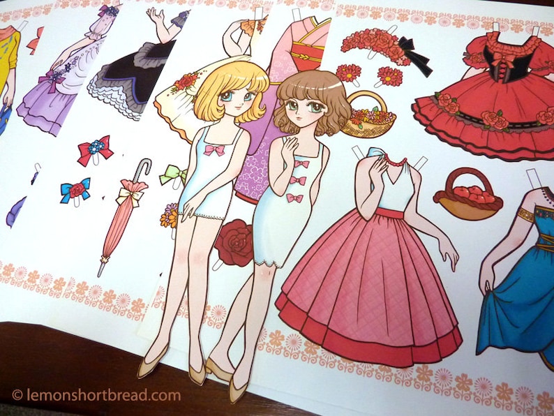 Puede incluir: Un conjunto de mu&ntilde;ecas de papel con dos mu&ntilde;ecas, cada una con varios atuendos y accesorios. Las mu&ntilde;ecas tienen el pelo largo y casta&ntilde;o y llevan vestidos blancos. Los atuendos incluyen un vestido rojo, un vestido rosa, un vestido azul y un vestido blanco con estampado floral. Los accesorios incluyen una cesta de flores, una cesta de manzanas, una corona de flores y una sombrilla.