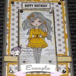 May include: A birthday card with a whimsical illustration of a girl with long gray hair wearing a yellow dress and holding a wand. The card has a gold glitter border and the words "HAPPY BIRTHDAY" at the top. The card also includes the text "Designed by Kym Upshaw" and "Lemon Shortbread".