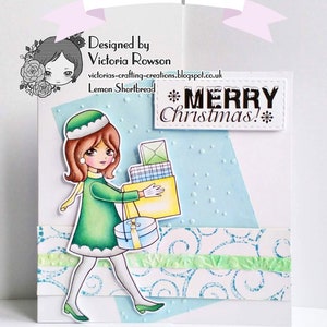 K&ouml;nnte beinhalten: Eine Weihnachtskarte mit einem Cartoon-M&auml;dchen in einem gr&uuml;nen Mantel, das Geschenke tr&auml;gt. Die Karte hat einen blauen Hintergrund mit wei&szlig;en Punkten und den Text "Frohe Weihnachten!" in Schwarz.