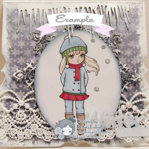 May include: A winter-themed card with a girl wearing a blue coat, red scarf, and green and white hat. The card has a white lace border and a snowflake pattern background. The text "Designed by Bettina Leikvoll" and "Lemon Shortbread" is at the bottom of the card.