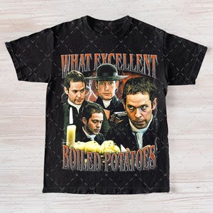 May include: Black t-shirt featuring a graphic print of four men and the text "What Excellent Boiled Potatoes".