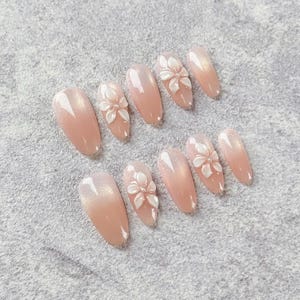 Schicke weiche rosa Mandelpresse auf den Nagel, zarte weiße Blumenkunst mit subtilem Glanz, eleganter künstlicher Nagel für Hochzeiten und lässige Glam-Looks
