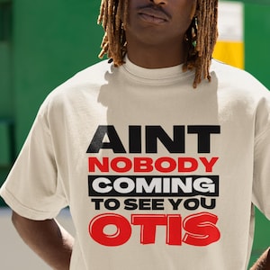 Pode incluir: Uma camiseta branca com texto preto e vermelho que diz "Ain't nobody coming to see you Otis".