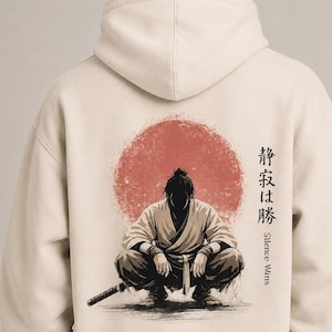 May include: A beige hooded sweatshirt featuring a graphic on the back of a crouching figure in traditional attire before a large red circle. The design includes Japanese characters and the English text "Silence Wins" printed vertically on the right.