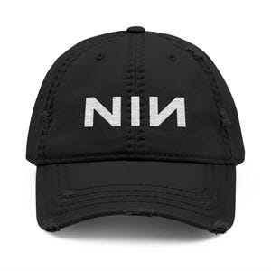 May include: Black distressed baseball cap featuring the white letters "NIN". The cap has a curved peak and a worn, distressed appearance.