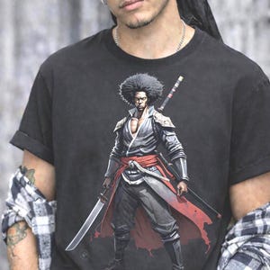 May include: A black short-sleeve t-shirt featuring a graphic print of a warrior with an afro hairstyle, wearing a dark jacket and red sash, holding a katana sword. The warrior is depicted in a standing pose with a sword strapped to their back.