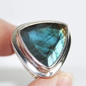 May include: A silver ring featuring a triangular blue labradorite gemstone. The ring has a plain band with a double border around the stone.