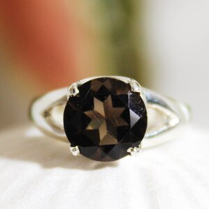 May include: A silver ring featuring a dark brown gemstone. The gemstone is round and has a faceted cut.