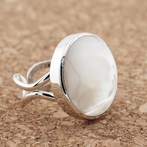 May include: A silver ring with a white mother-of-pearl stone set in a round bezel.