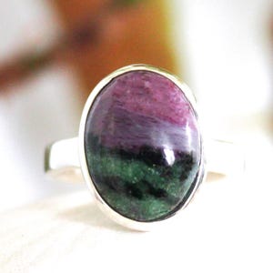 May include: A silver ring with an oval gemstone. The stone displays a colour gradient, starting with magenta, transitioning to purple, and ending with green. The ring's band is made of polished silver. The gemstone is set in a silver bezel.