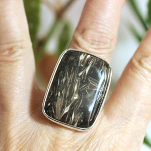 May include: A silver ring with a rectangular black and white stone. The stone has a unique pattern of white lines and swirls.
