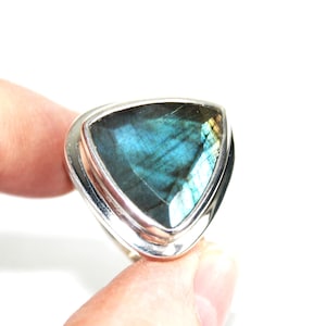 May include: A silver ring with a triangular labradorite gemstone. The stone has iridescent colours of blue, green, and yellow. The ring has a simple, polished silver band and bezel setting, highlighting the gemstone's unique colour.
