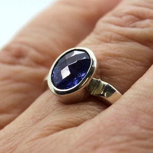 Peut inclure: Une bague en argent avec une pierre précieuse ovale bleu foncé sertie dans un sertissage à bélière.
