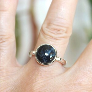 May include: A silver ring featuring a large, round, dark blue gemstone with lighter blue and white streaks. The ring is set in a simple, polished silver band.