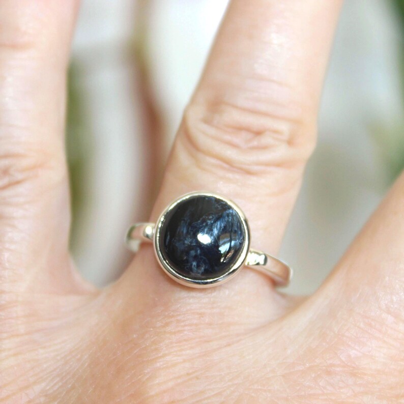 May include: A silver ring featuring a large, round, dark blue gemstone with lighter blue and white streaks. The ring is set in a simple, polished silver band.