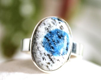 Peut inclure: Bague en argent ornée d'une pierre k2 ovale. La pierre présente une base blanche parsemée de taches noires et un centre bleu vif. Le corps de la bague est en argent poli.