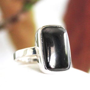 May include: A silver ring featuring a large, rectangular black stone. The stone is set in a polished silver band, creating a striking contrast. The ring's design is simple yet elegant, suitable for everyday wear or special occasions.