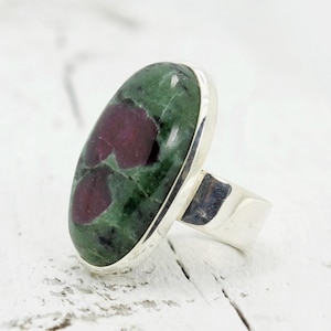 May include: A silver ring featuring a large oval green and pink gemstone. The gemstone has a mottled pattern of green and pink.