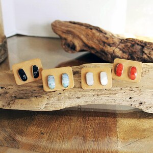 May include: Five pairs of oval-shaped earrings with different colored stones. The earrings are displayed on small brown cards. The stones are black, blue, white, red, and orange.