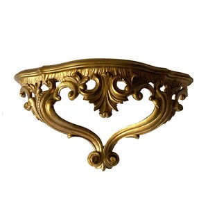 May include: A gold-colored, ornate, decorative wall shelf with a curved top and intricate scrollwork.