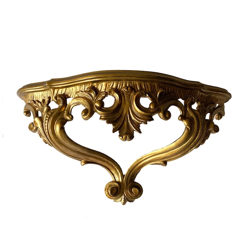 May include: A gold-colored, ornate, decorative wall shelf with a curved top and intricate scrollwork.