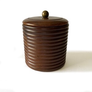 May include: A dark brown wooden ice bucket with a brass knob on the lid. The bucket is made of stacked rings of wood.