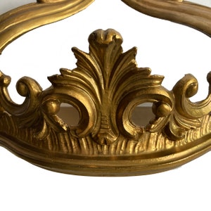 May include: Gold-toned metal crown-shaped decorative piece with intricate scrollwork and floral details.