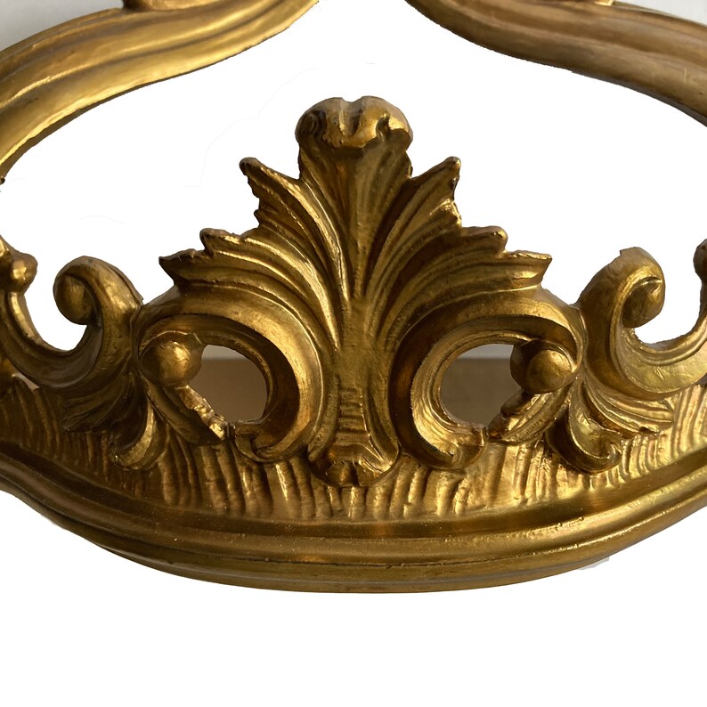 May include: Gold-toned metal crown-shaped decorative piece with intricate scrollwork and floral details.