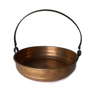 May include: A copper serving bowl with a hammered finish and a black metal handle. The bowl is round and has a wide rim.