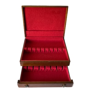 Può includere: Una scatola per posate in legno con un interno in velluto rosso. La scatola ha un coperchio incernierato e un cassetto. Il cassetto è rivestito in velluto rosso ed è diviso in scomparti per riporre le posate.