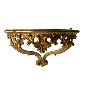 May include: A gold-colored, ornate, decorative wall shelf with a half-circle shape and intricate scrollwork.