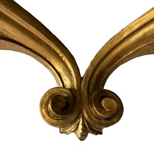 May include: A pair of ornate, gold-painted, wooden scrollwork brackets. The brackets are joined at the bottom with a decorative, swirling design.