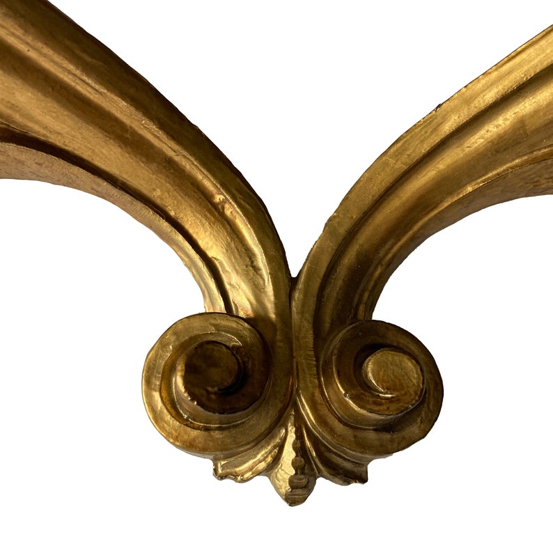 May include: A pair of ornate, gold-painted, wooden scrollwork brackets. The brackets are joined at the bottom with a decorative, swirling design.