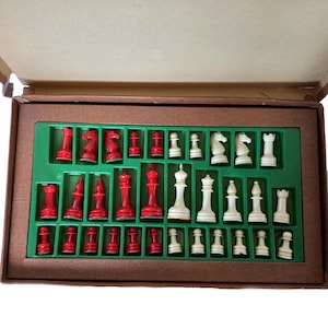 May include: A complete chess set with red and white pieces, neatly arranged in a green tray within a brown case. The pieces include rooks, knights, bishops, a king, a queen, and pawns. The case is open, revealing the full set.