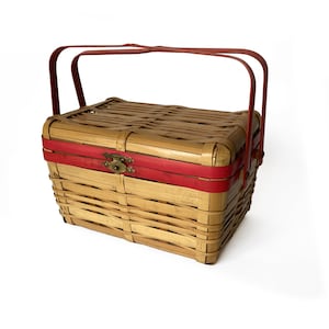 May include: A woven bamboo picnic basket with a red handle and a red band around the top. The basket has a brass latch.