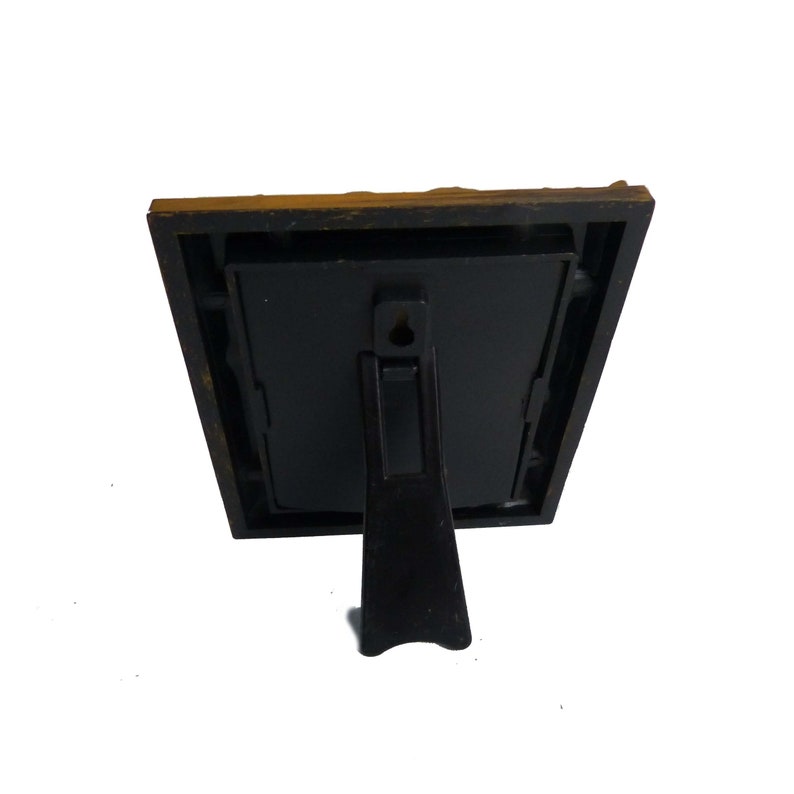 May include: A black picture frame with a gold-colored border and a stand on the back. The frame is made of plastic and has a simple design.