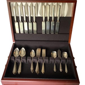 May include: A wooden box with a black velvet interior containing a set of silver flatware. The flatware includes knives, forks, and spoons.